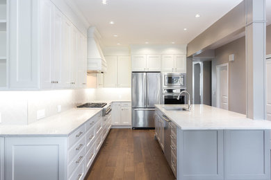 Example of a large transitional l-shaped dark wood floor and brown floor enclosed kitchen design in Vancouver with an undermount sink, recessed-panel cabinets, white cabinets, marble countertops, white backsplash, porcelain backsplash, stainless steel appliances and a peninsula