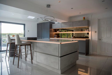 This is an example of a mid-sized modern galley open plan kitchen in Other with an undermount sink, flat-panel cabinets, grey cabinets, quartzite benchtops, black splashback, glass sheet splashback, black appliances, porcelain floors, with island, grey floor and beige benchtop.