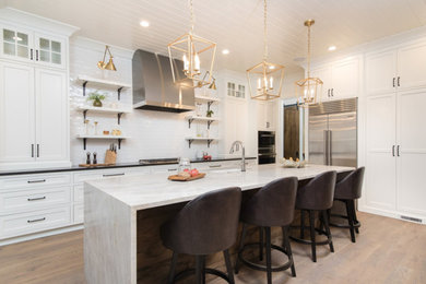 Contemporary eat-in kitchen in Dallas with a drop-in sink, recessed-panel cabinets, white cabinets, granite benchtops, white splashback, glass sheet splashback, stainless steel appliances, light hardwood floors, with island, beige floor and black benchtop.