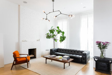 This is an example of a scandinavian open concept living room in New York with white walls, light hardwood floors, a standard fireplace, a brick fireplace surround and no tv.