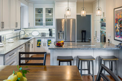 Example of a transitional l-shaped medium tone wood floor and brown floor kitchen design in Houston with an undermount sink, recessed-panel cabinets, white cabinets, gray backsplash, mosaic tile backsplash, stainless steel appliances, a peninsula and gray countertops