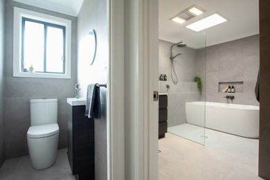 Large contemporary kids wet room bathroom in Sydney with flat-panel cabinets, dark wood cabinets, a corner tub, a two-piece toilet, gray tile, grey walls, an undermount sink, grey floor, an open shower, white benchtops, an enclosed toilet, a double vanity and a freestanding vanity.