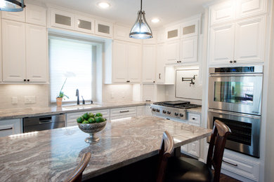 Example of a classic l-shaped porcelain tile and brown floor open concept kitchen design in Minneapolis with an undermount sink, raised-panel cabinets, white cabinets, granite countertops, white backsplash, stone tile backsplash, stainless steel appliances and an island