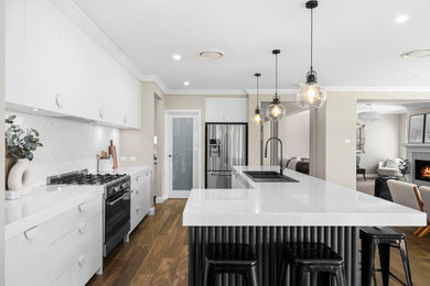 Design ideas for a mid-sized contemporary galley kitchen pantry in Sydney with a double-bowl sink, white cabinets, quartz benchtops, white splashback, ceramic splashback, stainless steel appliances, light hardwood floors, with island, brown floor and white benchtop.