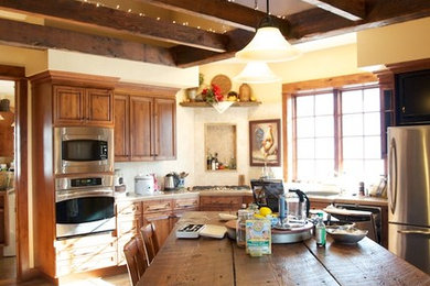 Example of a large mountain style l-shaped medium tone wood floor enclosed kitchen design in Other with raised-panel cabinets, medium tone wood cabinets, an island, solid surface countertops, stainless steel appliances and a drop-in sink