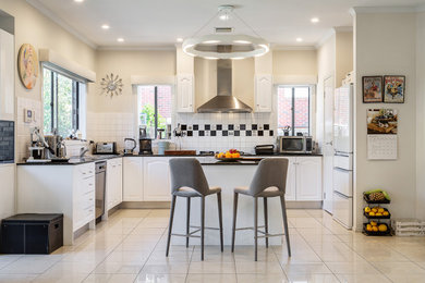 This is an example of a mid-sized eclectic eat-in kitchen in Melbourne with a double-bowl sink, beaded inset cabinets, white cabinets, marble benchtops, white splashback, ceramic splashback, stainless steel appliances, terra-cotta floors, with island, white floor and black benchtop.