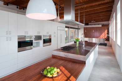 Minimalist concrete floor kitchen photo in Chicago with an undermount sink, flat-panel cabinets, white cabinets, wood countertops, stainless steel appliances and an island