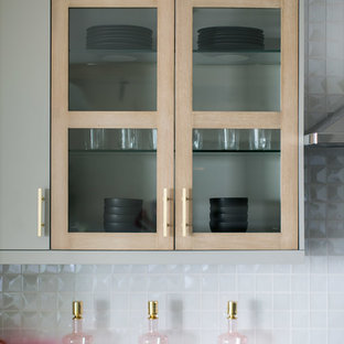 Inredning av ett stort kök, med en nedsänkt diskho, släta luckor, grå skåp, marmorbänkskiva, vitt stänkskydd, stänkskydd i glaskakel, rostfria vitvaror, kalkstensgolv och en köksö