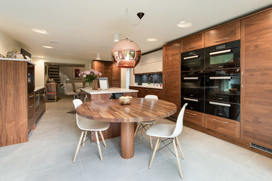 Large traditional u-shaped kitchen/diner in Buckinghamshire with a submerged sink, shaker cabinets, medium wood cabinets, quartz worktops, blue splashback, glass sheet splashback, black appliances, porcelain flooring, an island, grey floors and white worktops.