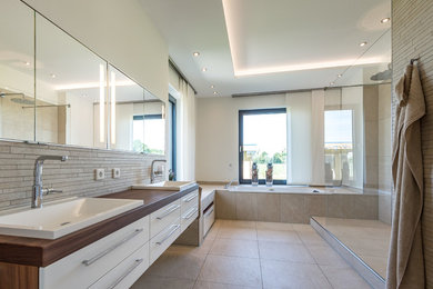 Foto de cuarto de baño actual grande con puertas de armario blancas, paredes blancas, encimera de madera y bañera encastrada