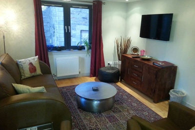 Ejemplo de sala de estar abierta clásica renovada pequeña con paredes grises, suelo de madera clara, televisor colgado en la pared y suelo marrón