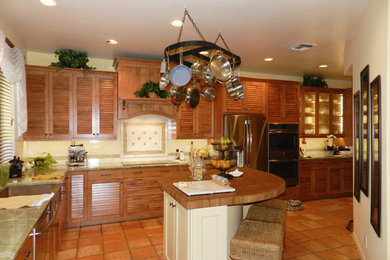 Large island style l-shaped terra-cotta tile and brown floor kitchen photo in Miami with a farmhouse sink, louvered cabinets, medium tone wood cabinets, white backsplash, ceramic backsplash, stainless steel appliances and an island