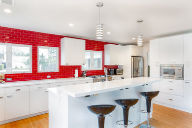Large modern single-wall eat-in kitchen in Orange County with an undermount sink, flat-panel cabinets, white cabinets, quartz benchtops, red splashback, glass tile splashback, stainless steel appliances, medium hardwood floors, with island, brown floor and white benchtop.
