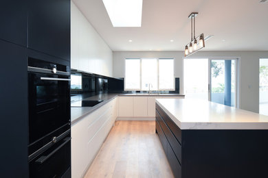 This is an example of a large contemporary galley eat-in kitchen in Sydney with an undermount sink, flat-panel cabinets, quartz benchtops, black splashback, mirror splashback, black appliances, medium hardwood floors, with island, brown floor and yellow benchtop.