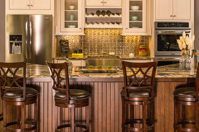 Mid-sized elegant galley travertine floor enclosed kitchen photo in Denver with raised-panel cabinets, beige cabinets, granite countertops, metallic backsplash, metal backsplash, stainless steel appliances and an island