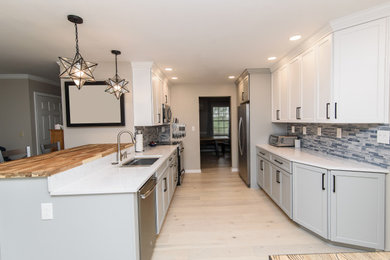 Example of a mid-sized transitional u-shaped enclosed kitchen design in Baltimore with an undermount sink, shaker cabinets, white cabinets, quartz countertops, blue backsplash, subway tile backsplash, stainless steel appliances, a peninsula and white countertops