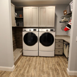 This is an example of a medium sized traditional galley utility room with flat-panel cabinets, grey cabinets, engineered stone countertops, grey walls, laminate floors, a side by side washer and dryer and brown floors.