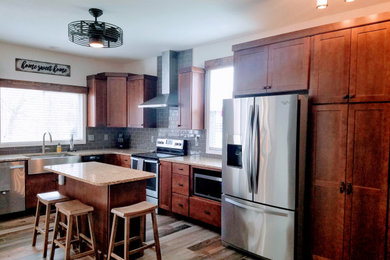 Mid-sized country l-shaped ceramic tile and brown floor kitchen photo in Kansas City with a farmhouse sink, shaker cabinets, medium tone wood cabinets, granite countertops, gray backsplash, subway tile backsplash, stainless steel appliances, an island and multicolored countertops