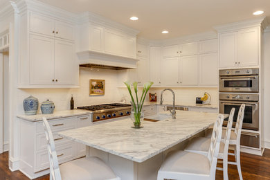 Design ideas for a mid-sized traditional l-shaped separate kitchen in Raleigh with a farmhouse sink, beaded inset cabinets, white cabinets, marble benchtops, white splashback, ceramic splashback, stainless steel appliances, medium hardwood floors, with island, brown floor and white benchtop.
