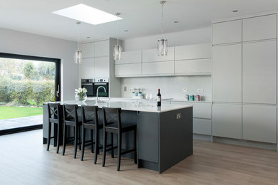 This is an example of an expansive contemporary single-wall open plan kitchen in Other with an integrated sink, flat-panel cabinets, grey cabinets, quartzite benchtops, white splashback, stone slab splashback, stainless steel appliances, medium hardwood floors, with island, brown floor and white benchtop.