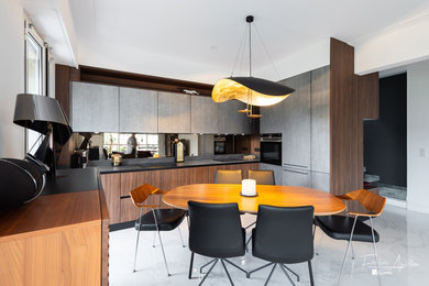 Idée de décoration pour une grande cuisine américaine vintage en U et bois brun avec un évier intégré, un placard à porte affleurante, un plan de travail en quartz, une crédence marron, une crédence en bois, un électroménager noir, un sol en marbre, aucun îlot, un sol gris et plan de travail noir.