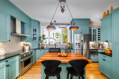 Enclosed kitchen - mid-sized victorian u-shaped medium tone wood floor enclosed kitchen idea in Boston with a farmhouse sink, recessed-panel cabinets, turquoise cabinets, soapstone countertops, white backsplash, ceramic backsplash, stainless steel appliances, an island and black countertops