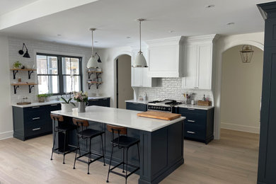 Example of a mid-sized trendy medium tone wood floor kitchen design in Montreal with a farmhouse sink, shaker cabinets, white cabinets, quartz countertops, white backsplash, ceramic backsplash, an island and white countertops