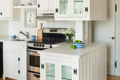Eat-in kitchen - small coastal l-shaped light wood floor eat-in kitchen idea in Boston with an undermount sink, glass-front cabinets, white cabinets, solid surface countertops, white backsplash, stone slab backsplash, stainless steel appliances and no island