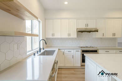 Example of a mid-sized minimalist l-shaped light wood floor and beige floor kitchen design in Los Angeles with a drop-in sink, shaker cabinets, white cabinets, solid surface countertops, white backsplash, porcelain backsplash, stainless steel appliances, an island and gray countertops