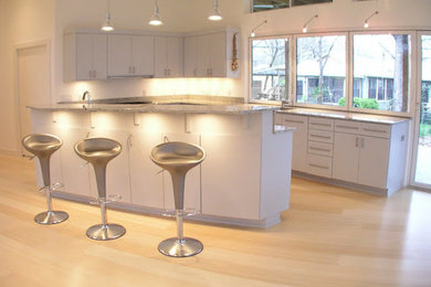 Example of a large l-shaped light wood floor kitchen design in Austin with an undermount sink, flat-panel cabinets, white cabinets, granite countertops, stainless steel appliances and an island