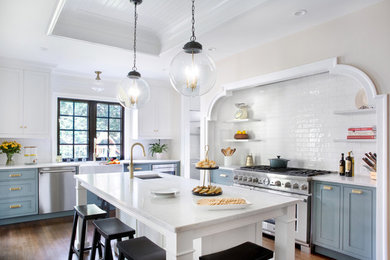 Inspiration for a mid-sized transitional l-shaped dark wood floor, brown floor and tray ceiling kitchen remodel in New York with a farmhouse sink, quartz countertops, white backsplash, ceramic backsplash, stainless steel appliances, an island, white countertops, beaded inset cabinets and blue cabinets