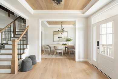 Large transitional light wood floor, tray ceiling and wood wall entryway photo in Philadelphia with beige walls and a white front door