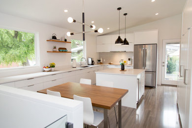 Large midcentury eat-in kitchen in Calgary with an undermount sink, flat-panel cabinets, white cabinets, quartzite benchtops, grey splashback, porcelain splashback, stainless steel appliances, laminate floors, with island, grey floor, white benchtop and vaulted.