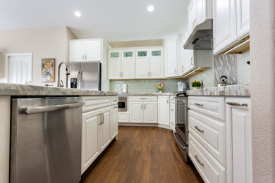 Example of a large classic l-shaped medium tone wood floor and brown floor kitchen pantry design in Other with an undermount sink, raised-panel cabinets, white cabinets, granite countertops, green backsplash, ceramic backsplash, stainless steel appliances, an island and green countertops