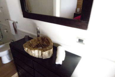 Mid-sized modern powder room in Catania-Palermo with furniture-like cabinets, dark wood cabinets, a two-piece toilet, white tile, porcelain tile, white walls, light hardwood floors, a vessel sink and wood benchtops.