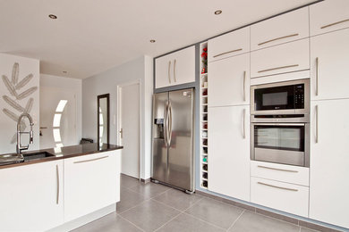 Cette image montre une grande cuisine américaine encastrable design avec un évier encastré, un placard à porte plane, des portes de placard blanches, un plan de travail en granite, un sol en carrelage de céramique, îlot et un sol gris.