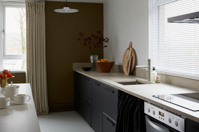 This is an example of a small contemporary galley enclosed kitchen in London with a single-bowl sink, flat-panel cabinets, black cabinets, concrete worktops, beige splashback, cement tile splashback and beige worktops.