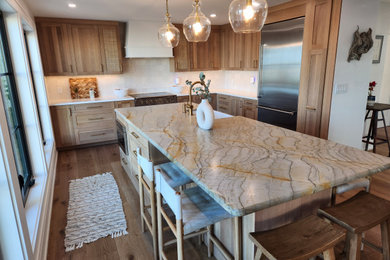 Large transitional l-shaped laminate floor and brown floor open concept kitchen photo in Tampa with a farmhouse sink, shaker cabinets, medium tone wood cabinets, quartzite countertops, white backsplash, ceramic backsplash, stainless steel appliances, an island and multicolored countertops