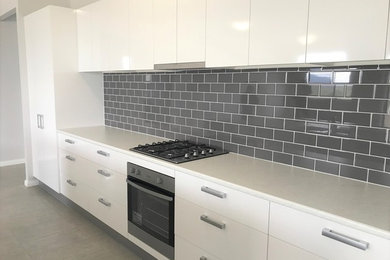 Photo of a modern galley eat-in kitchen in Newcastle - Maitland with a double-bowl sink, white cabinets, quartzite benchtops, grey splashback, subway tile splashback, stainless steel appliances, with island and grey floor.