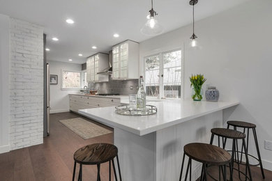Open concept kitchen - large transitional galley medium tone wood floor and brown floor open concept kitchen idea in Vancouver with a drop-in sink, raised-panel cabinets, white cabinets, quartzite countertops, gray backsplash, porcelain backsplash, stainless steel appliances and a peninsula