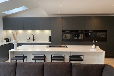 Design ideas for an expansive modern l-shaped open plan kitchen in Hampshire with a single-bowl sink, flat-panel cabinets, black cabinets, quartz worktops, white splashback, engineered quartz splashback, black appliances, an island, white worktops and a vaulted ceiling.