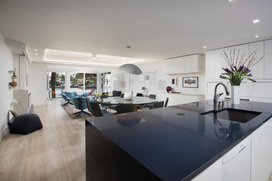 Design ideas for a mid-sized contemporary l-shaped open plan kitchen in Miami with an undermount sink, flat-panel cabinets, white cabinets, solid surface benchtops, multi-coloured splashback, porcelain splashback, white appliances, light hardwood floors, with island, beige floor and black benchtop.