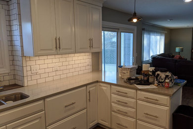 Design ideas for a mid-sized transitional u-shaped eat-in kitchen in Wichita with an undermount sink, raised-panel cabinets, white cabinets, quartz benchtops, white splashback, ceramic splashback, stainless steel appliances, a peninsula and grey benchtop.