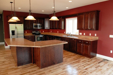 Mid-sized elegant l-shaped light wood floor and beige floor open concept kitchen photo in Other with a drop-in sink, raised-panel cabinets, dark wood cabinets, laminate countertops, stainless steel appliances and an island