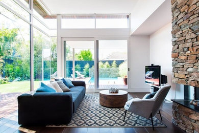 Modern open concept family room in Melbourne with white walls, medium hardwood floors, a corner fireplace, a stone fireplace surround and a freestanding tv.