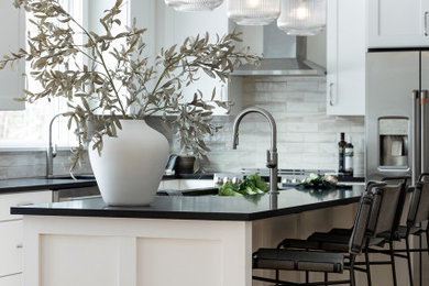 Large transitional u-shaped light wood floor and brown floor eat-in kitchen photo in Burlington with an undermount sink, shaker cabinets, white cabinets, granite countertops, gray backsplash, porcelain backsplash, stainless steel appliances, an island and black countertops