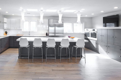 Example of a minimalist u-shaped medium tone wood floor and brown floor eat-in kitchen design in Oklahoma City with an undermount sink, flat-panel cabinets, gray cabinets, quartz countertops, white backsplash, porcelain backsplash, stainless steel appliances and an island