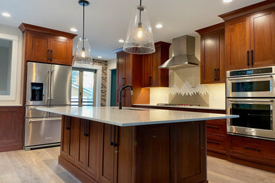 Inspiration for a large transitional l-shaped light wood floor and brown floor kitchen remodel in Denver with a drop-in sink, dark wood cabinets, marble countertops, white backsplash, ceramic backsplash, stainless steel appliances, an island and white countertops