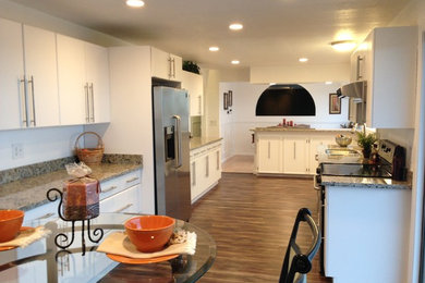Enclosed kitchen - mid-sized traditional u-shaped medium tone wood floor enclosed kitchen idea in Seattle with a double-bowl sink, flat-panel cabinets, white cabinets, granite countertops, stainless steel appliances and a peninsula