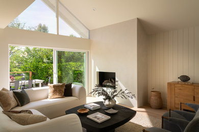 Example of a transitional open concept light wood floor, beige floor and vaulted ceiling living room design in Los Angeles with beige walls and a standard fireplace